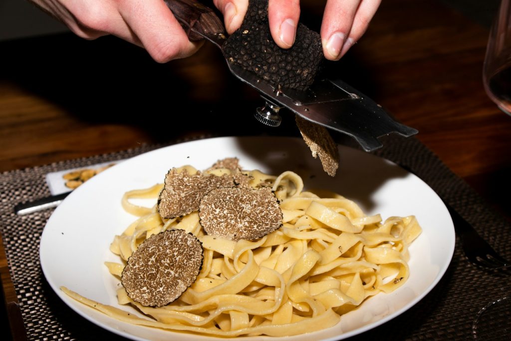 Chef cuisinier râpant des truffes d'été sur un plat de pâtes.